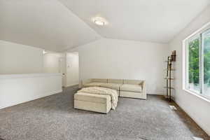 Vaulted ceiling living space featuring gray carpet flooring and ample natural light from the large window