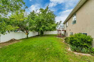Expansive backyard featuring a green lawn, mature trees, and a white privacy fence