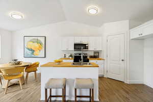Kitchen featuring white cabinetry, wood-finish countertops, stainless steel appliances, and a central island with integrated sink