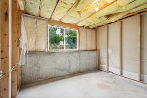 Unfinished lower level featuring exposed wood framing, a concrete foundation wall, and a window with exterior tree views