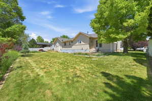 Expansive rear yard featuring mature trees, a manicured lawn, and perimeter landscaping