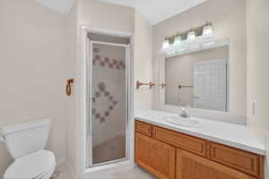 Main Level Bathroom featuring a glass-enclosed shower with decorative tile accents, a single vanity with a white countertop and integrated sink, and wood-finish cabinetry