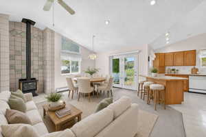 Virtual staging included to showcase room potential.  Open-concept living space featuring a tiled wood-burning stove, vaulted ceiling with recessed lighting, and a kitchen with wood cabinetry and a breakfast bar