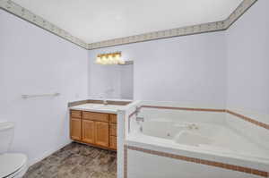 Primary Bathroom featuring a corner soaking tub with white tile surround, a single vanity with wood cabinetry, a light-toned countertop, and a wall-mounted mirror