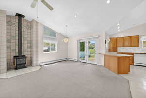 Vaulted ceiling great room with a tiled wood-burning stove, ceiling fan, and recessed lighting
