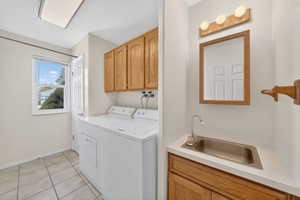 Utility room featuring tile flooring, a window, upper cabinetry, a utility sink with a countertop, and a vanity mirror with light fixture