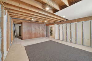 Unfinished basement space featuring exposed wood joists and structural beams, recessed lighting, concrete flooring, and partial wall framing for future customization