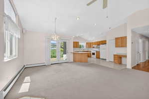 Carpeted open-concept living area featuring a kitchen with wood cabinetry and white appliances, vaulted ceilings, recessed lighting, and a ceiling fan