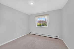 Neutral tone walls with soft carpet flooring, featuring a window with white trim, baseboard heating, and a recessed ceiling light fixture