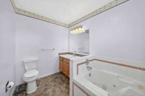 Primary Bathroom featuring a white jetted bathtub with tiled surround, a light wood-finish vanity with an integrated sink, a wall-mounted mirror, and tile flooring