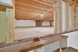 Crawlspace area. Unfinished basement offering exposed wood joists and structural beams, white perimeter walls, and a concrete floor