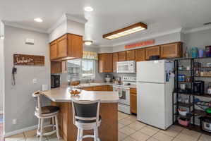 Kitchen featuring a breakfast bar with seating, wood cabinetry, white appliances, and tiled flooring