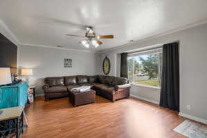 Spacious living area featuring wood-finish flooring, a large picture window with drapes, and a ceiling fan with integrated lighting