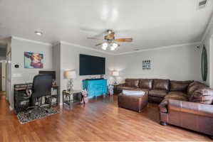 Spacious living area featuring laminate flooring, light gray walls, and white crown molding