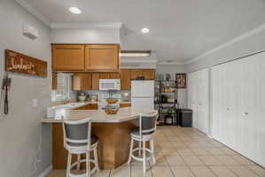 Kitchen featuring a peninsula, wood cabinetry, white appliances, and tiled flooring