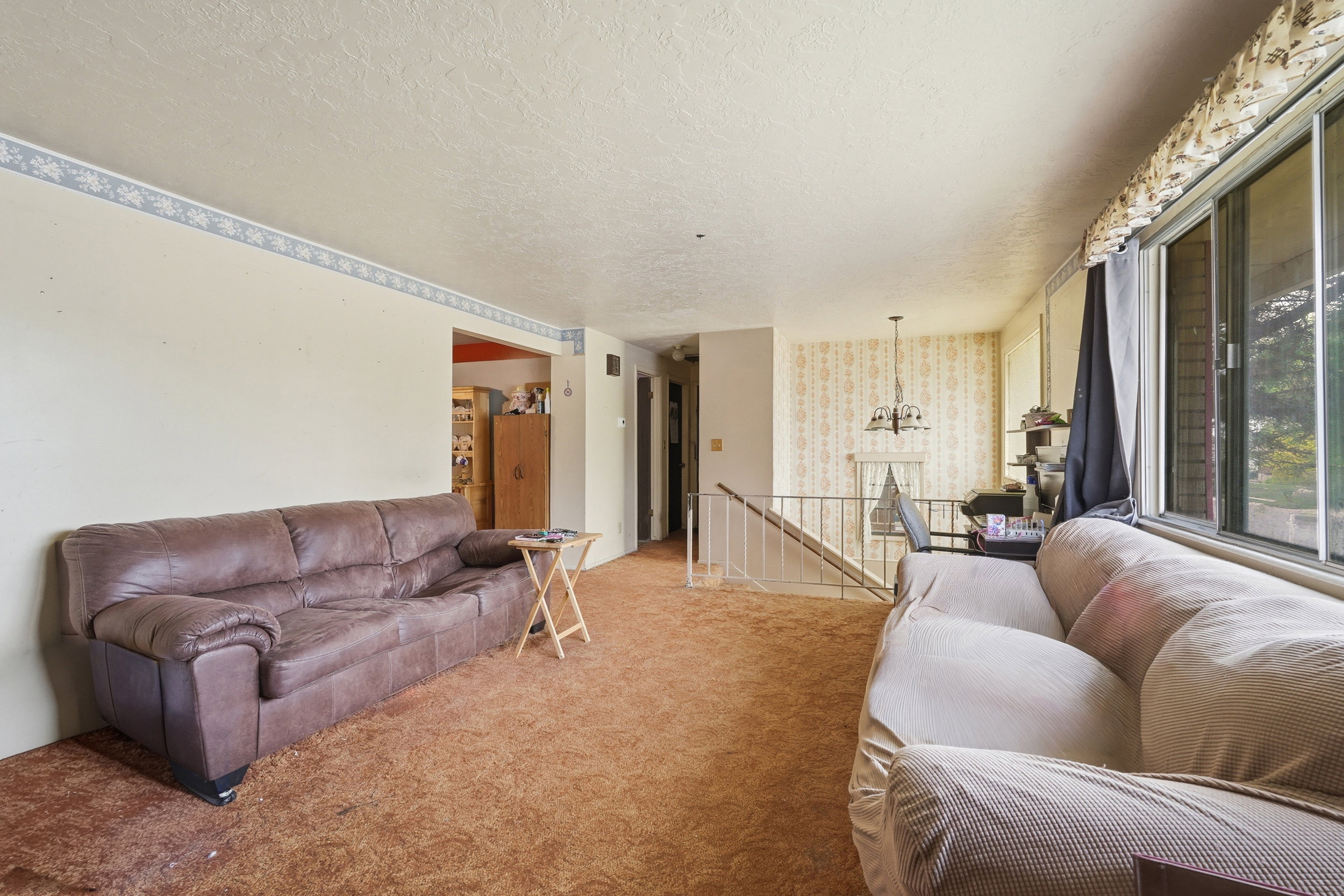 Spacious living area featuring expansive windows, textured ceilings, a decorative chandelier, and a white metal staircase railing