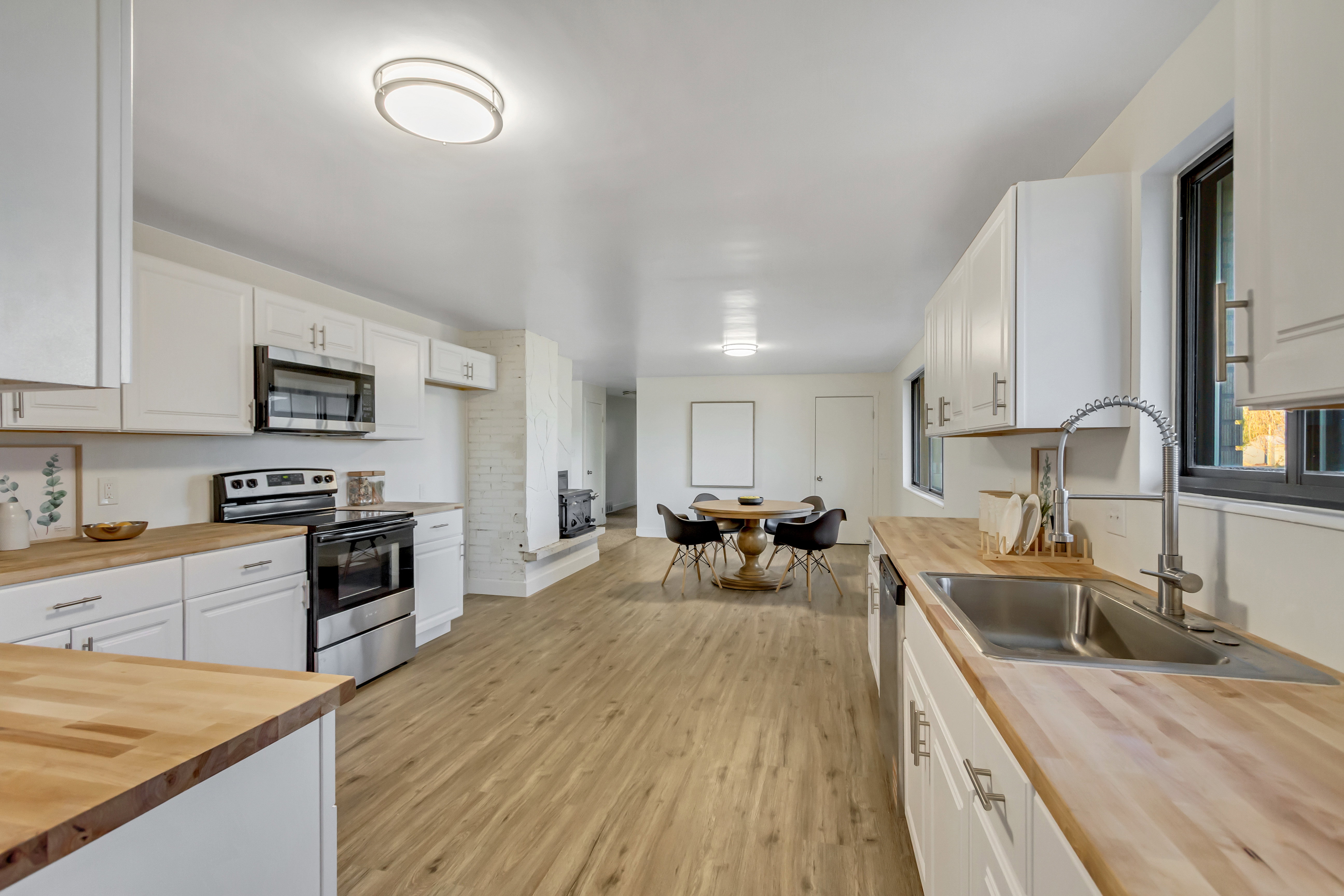 Bright kitchen featuring white cabinetry, butcher block countertops, stainless steel appliances, and wood-finish flooring