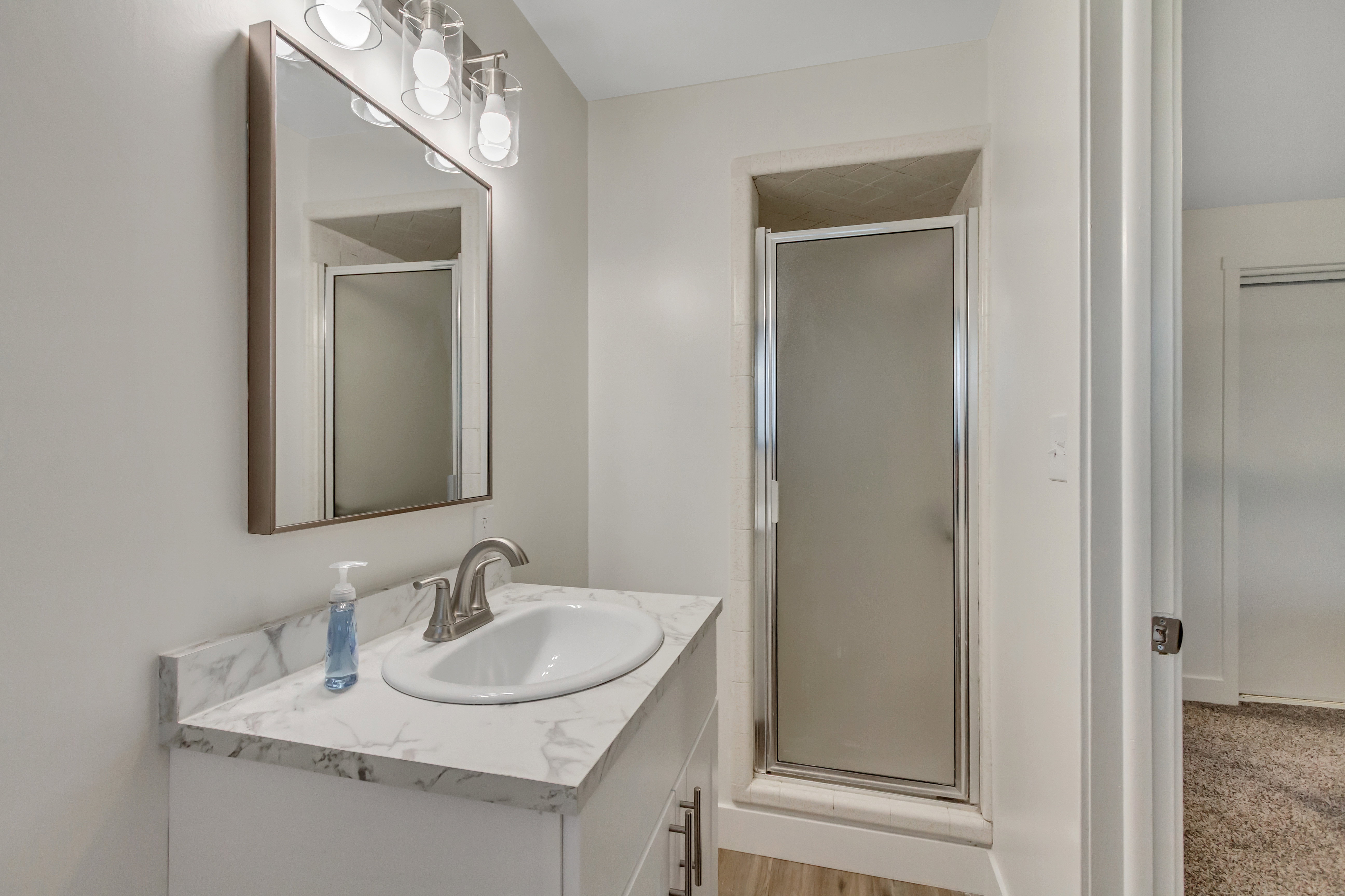 Bathroom featuring a single vanity with a white countertop and oval under-mount sink, brushed nickel faucet, and framed mirror with a three-light vanity fixture