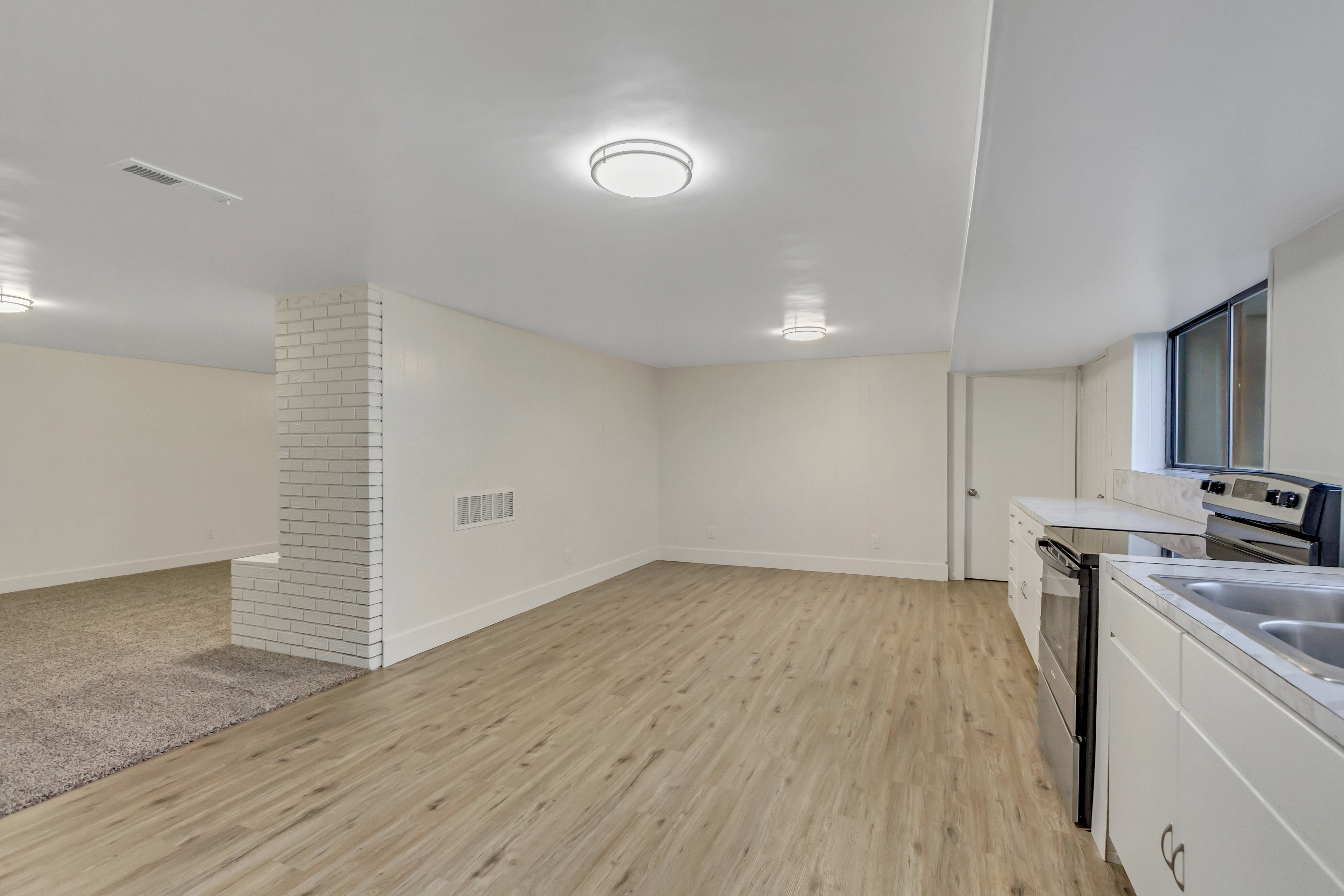 Open living area featuring wood-finish flooring, white cabinetry, a built-in electric range, and a double basin sink