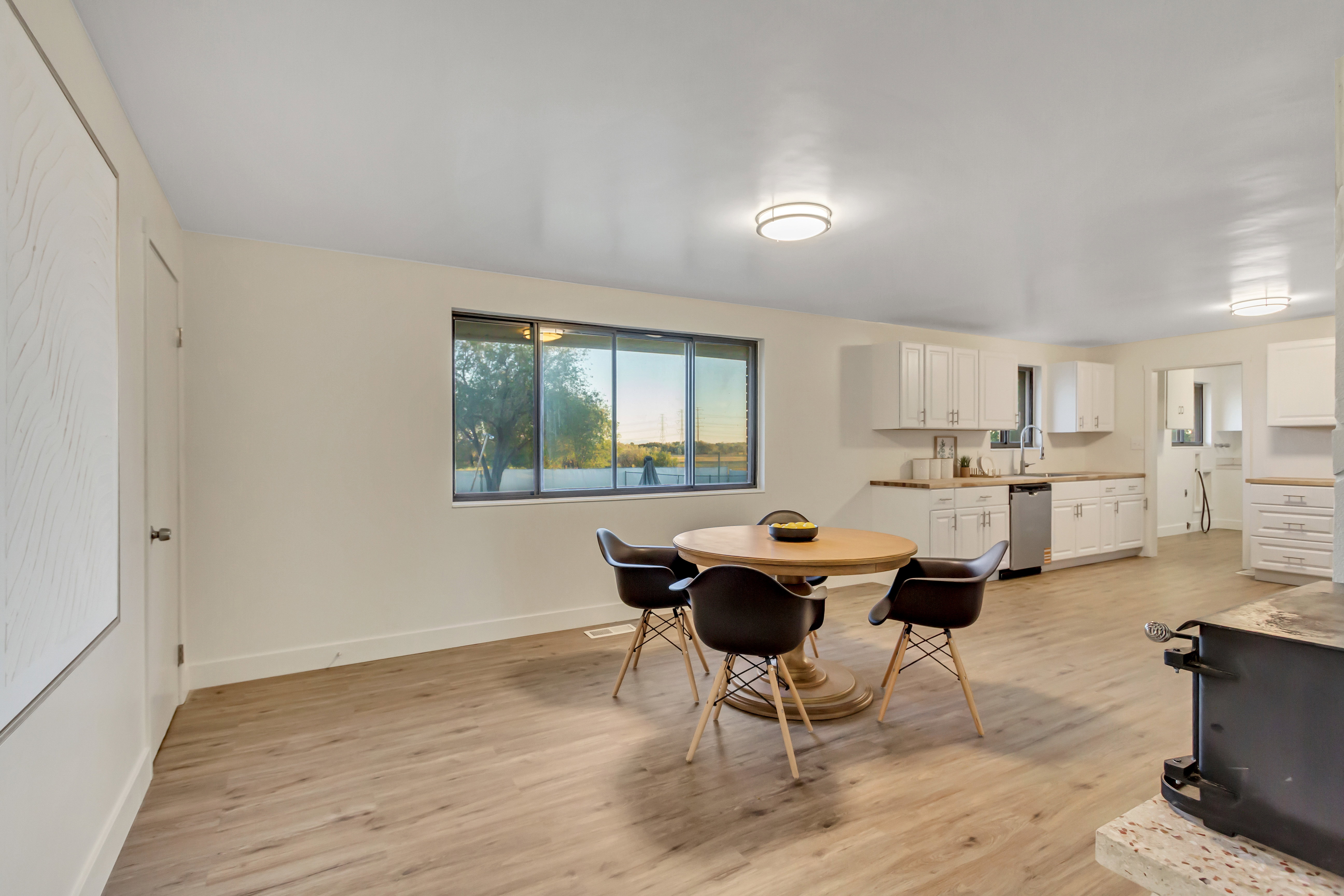 Open-concept living space featuring wood-finish flooring, a large window, white cabinetry, and a built-in kitchen sink