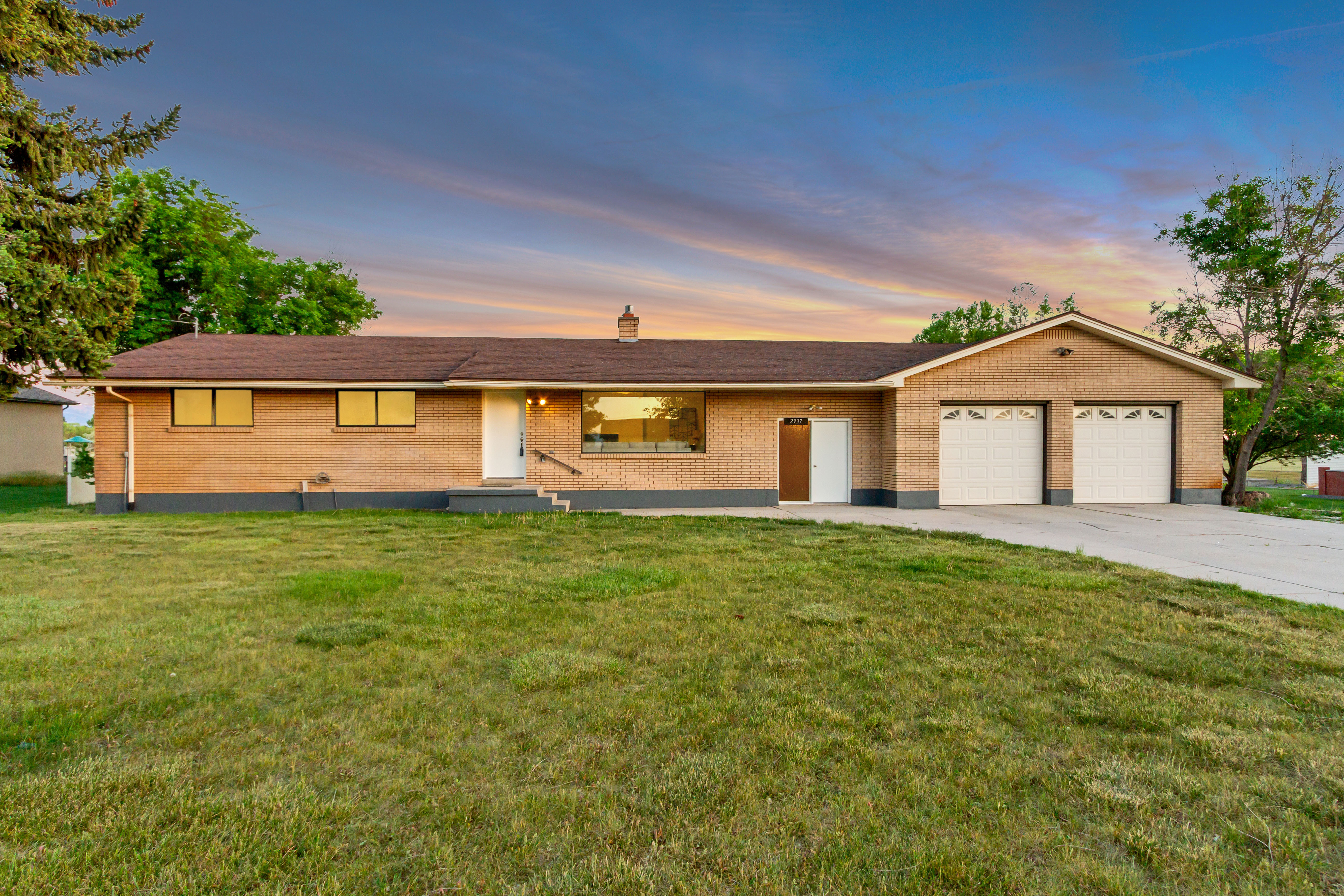 Brick exterior featuring a hip roof, integrated two-car garage with white paneled doors, and a concrete driveway