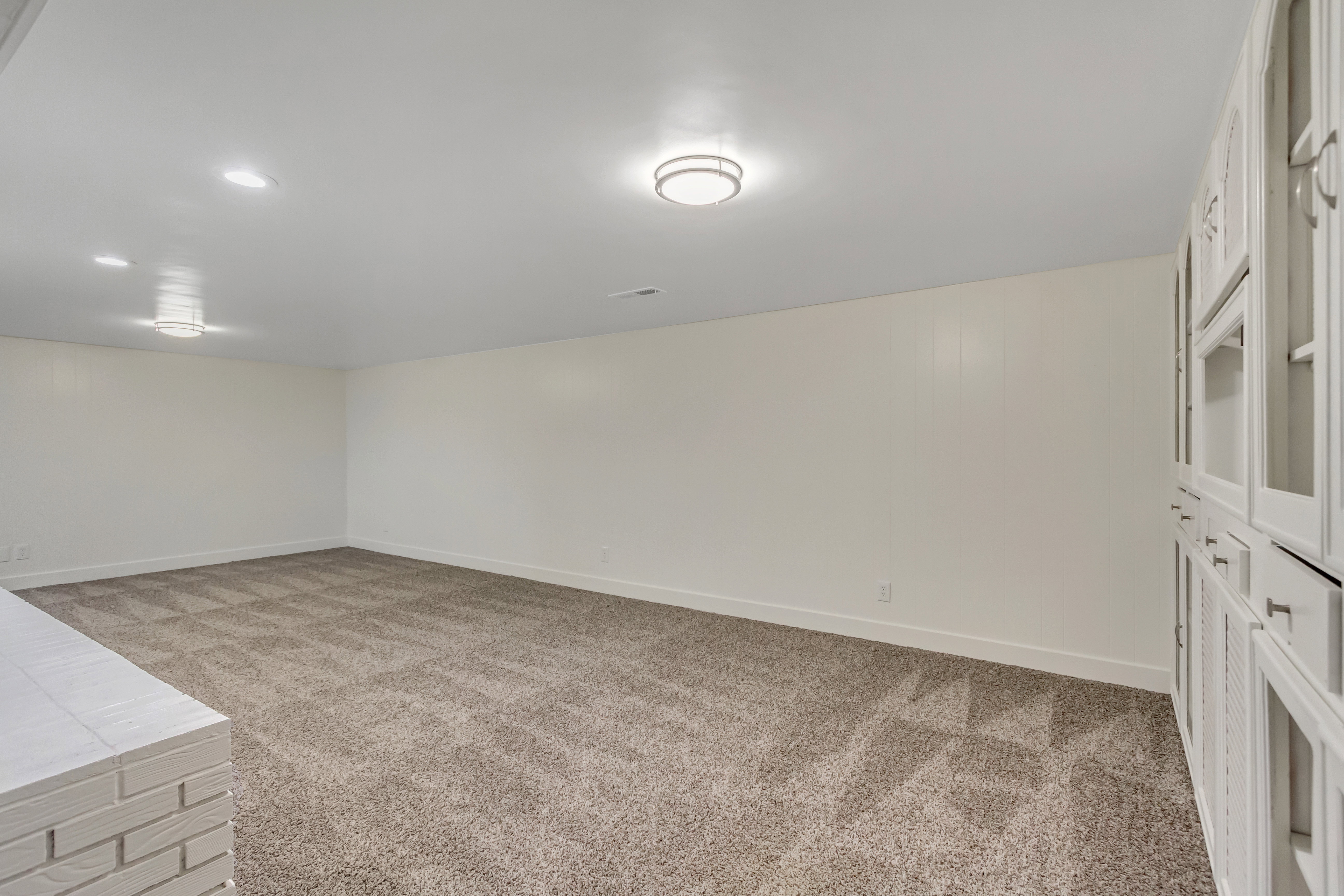 Spacious room featuring neutral carpet flooring, recessed lighting, and built-in cabinetry with glass panel doors