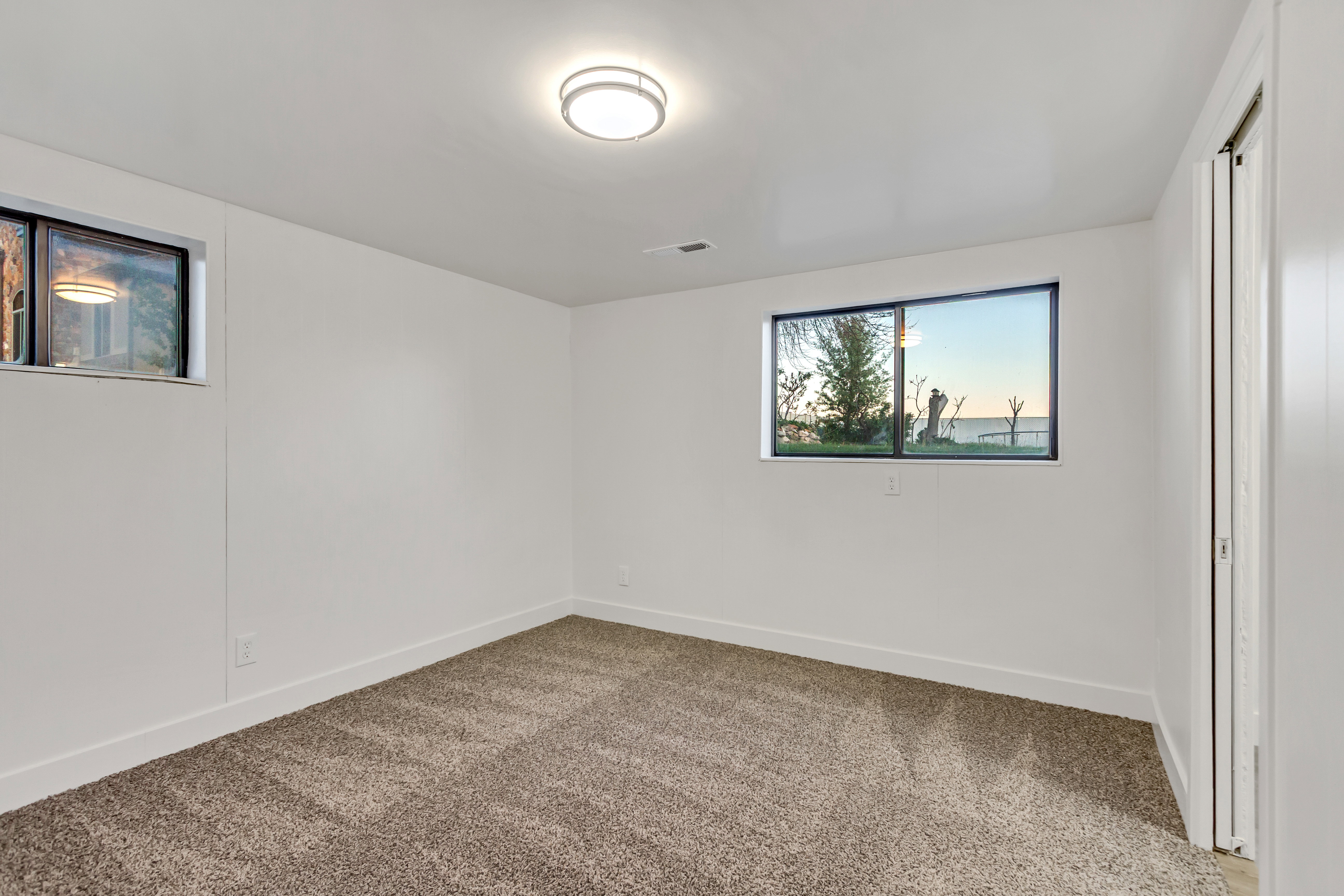 Carpeted room with white walls, a modern flush-mount ceiling light, and two windows providing natural illumination