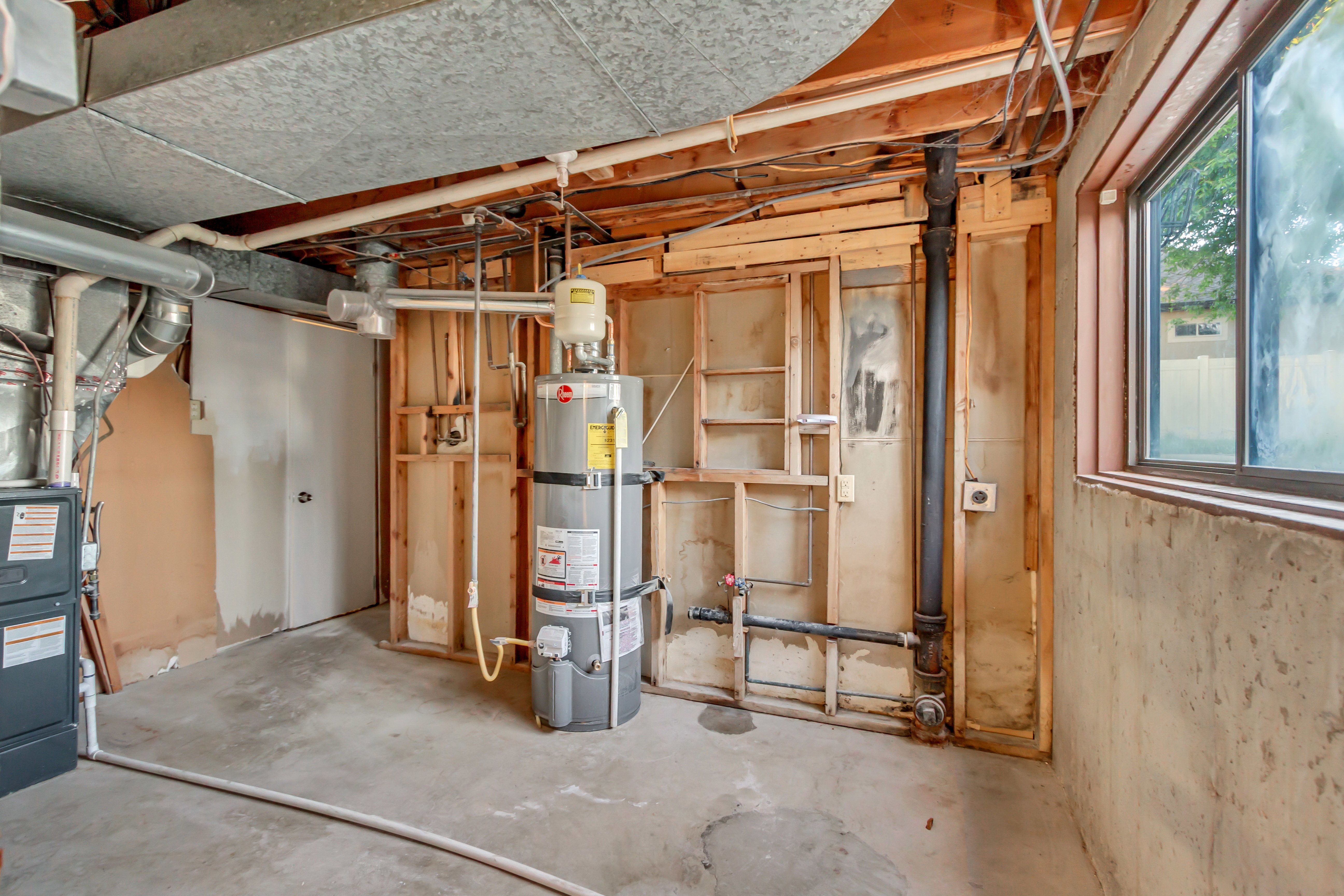 Utility room with exposed ceiling joists, concrete flooring, water heater, furnace, and a single window
