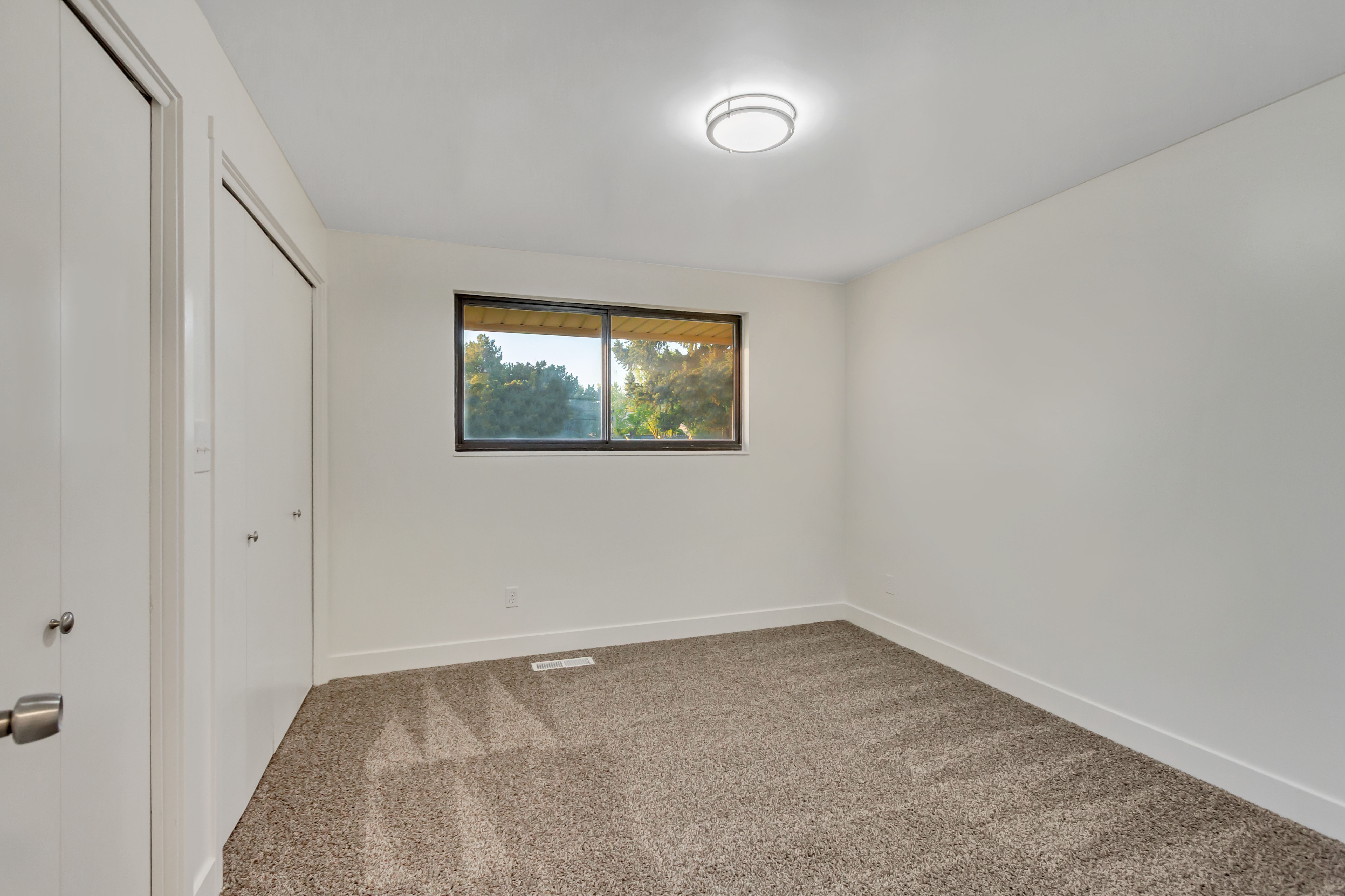 Carpeted room featuring a double closet with bi-fold doors, a single window, white baseboards, and a flush-mount ceiling light fixture