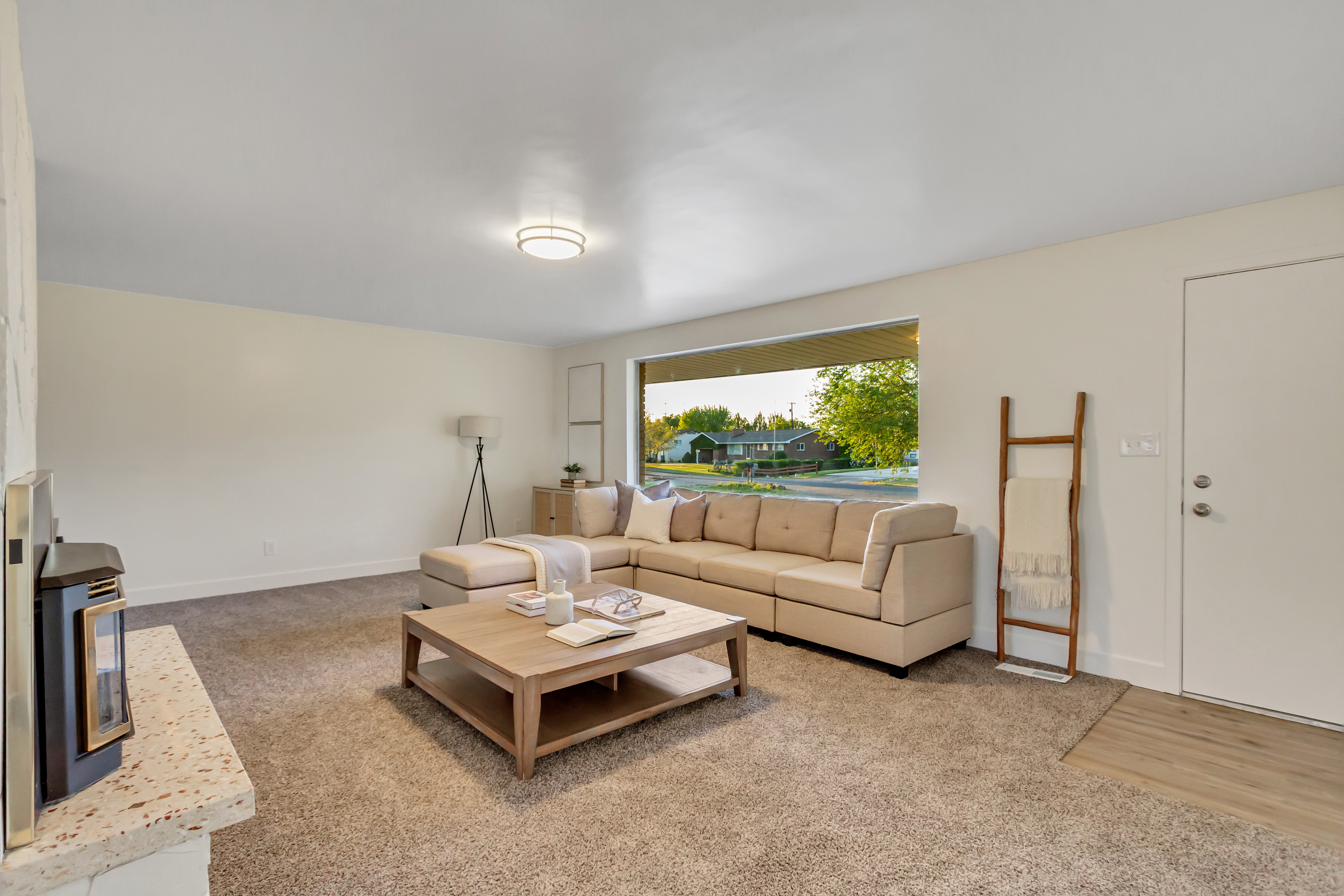 Living area featuring a large picture window, carpet flooring, a built-in fireplace with a light-colored hearth, and a modern flush-mount ceiling light