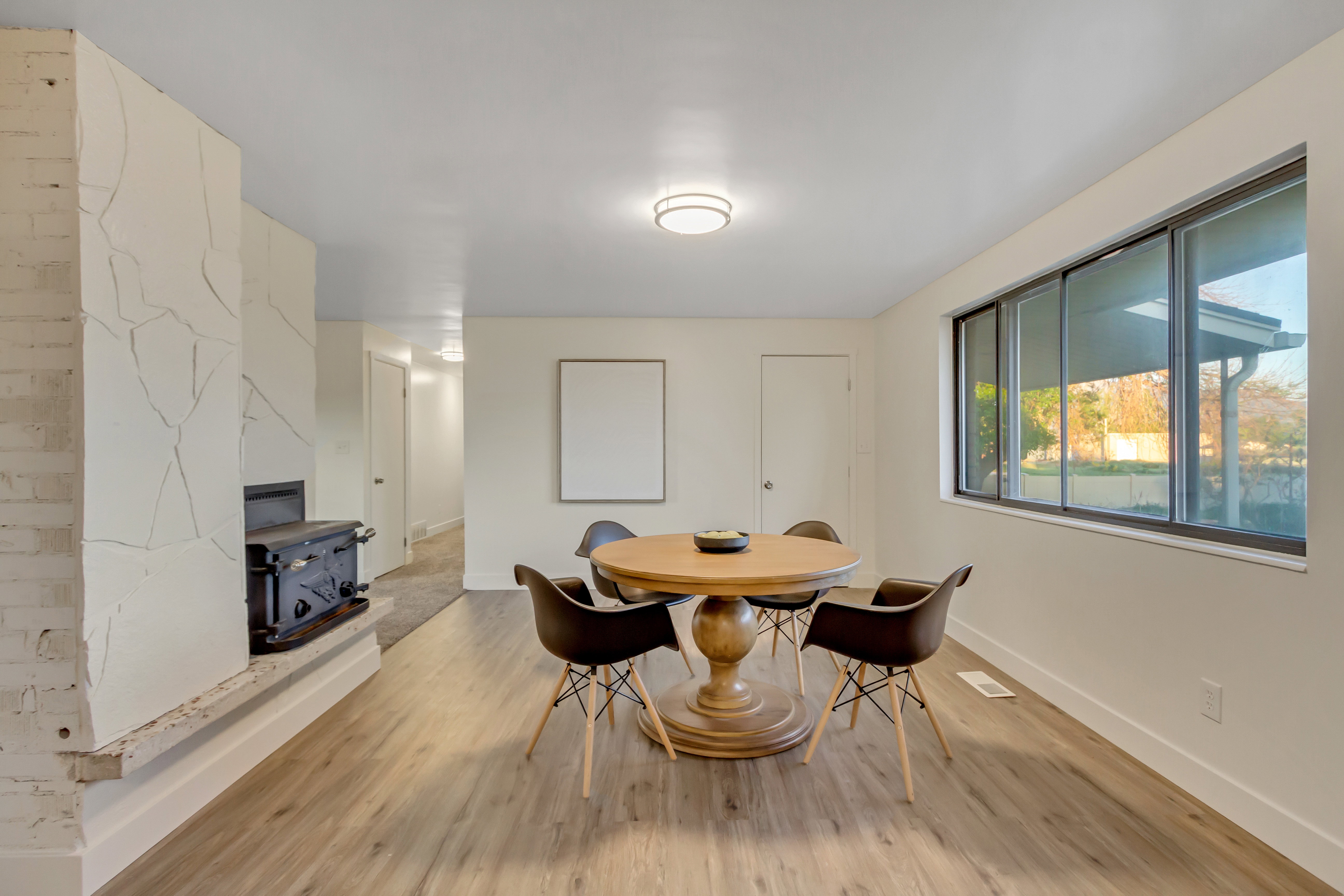 Spacious room featuring wood-finish flooring, a prominent stone-clad fireplace with a wood-burning stove, and a large multi-pane window
