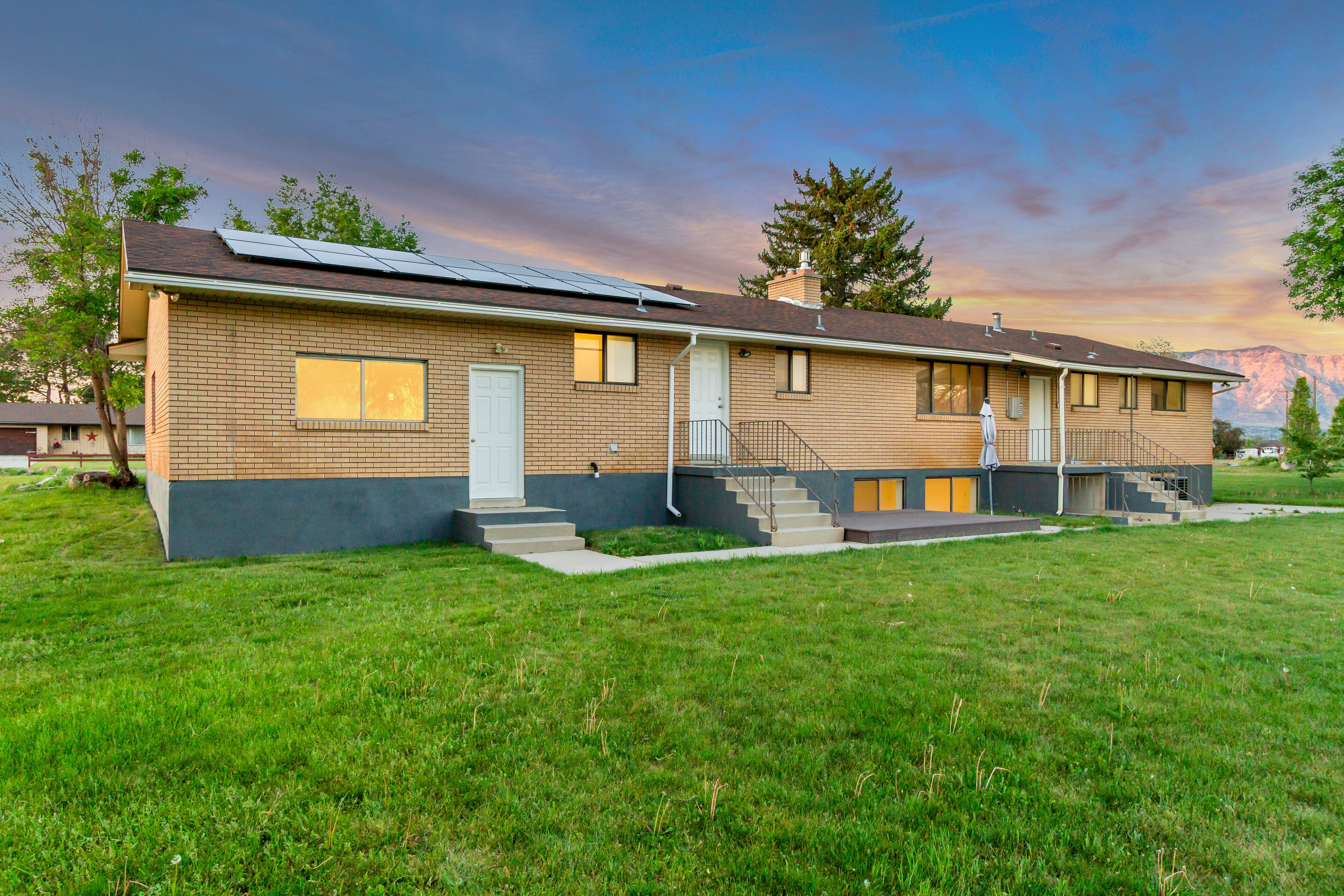 Expansive green lawn surrounds a brick exterior property featuring multiple entryways and solar panels
