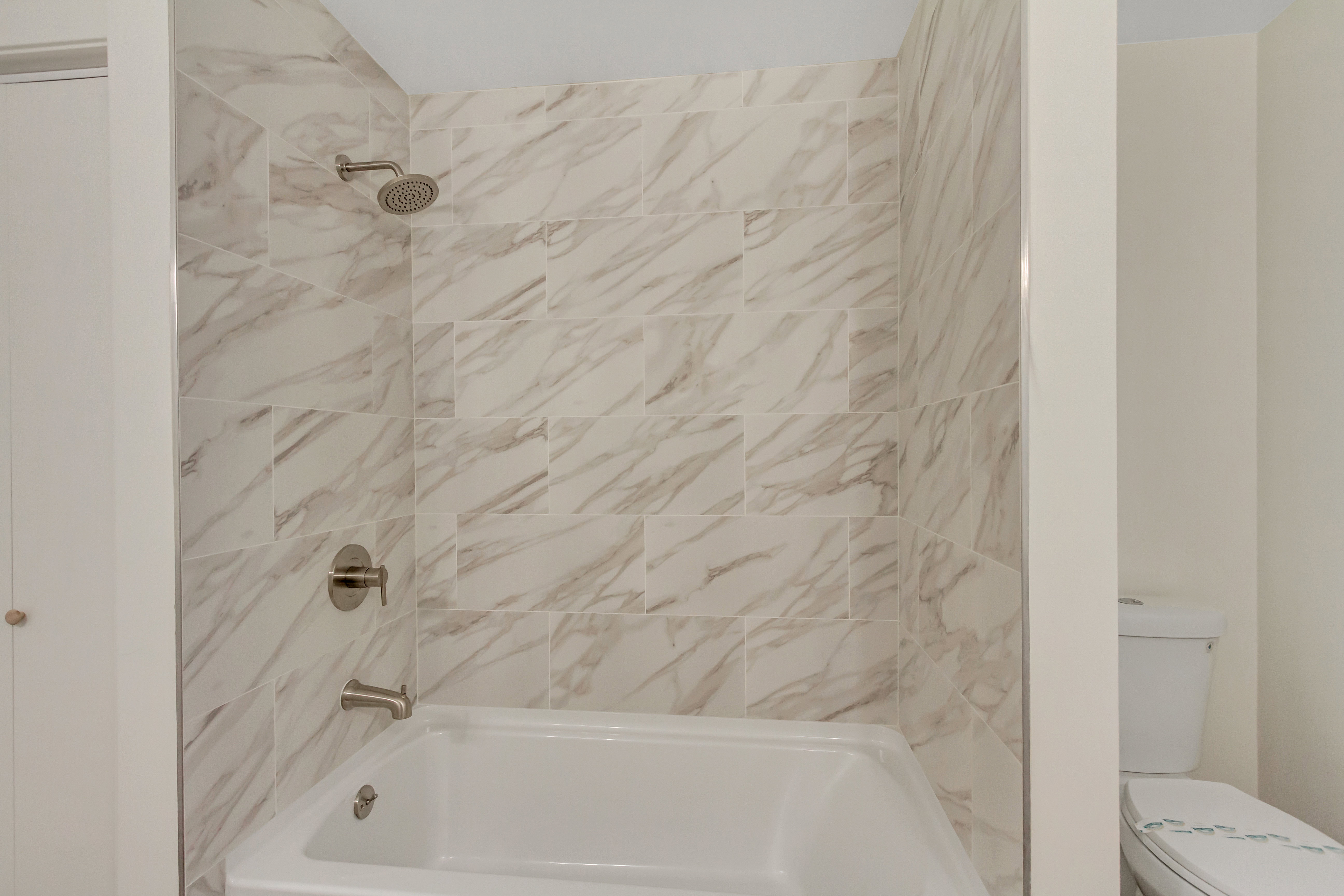 Bathtub with tiled shower surround featuring a rain-style shower head and a separate tub spout