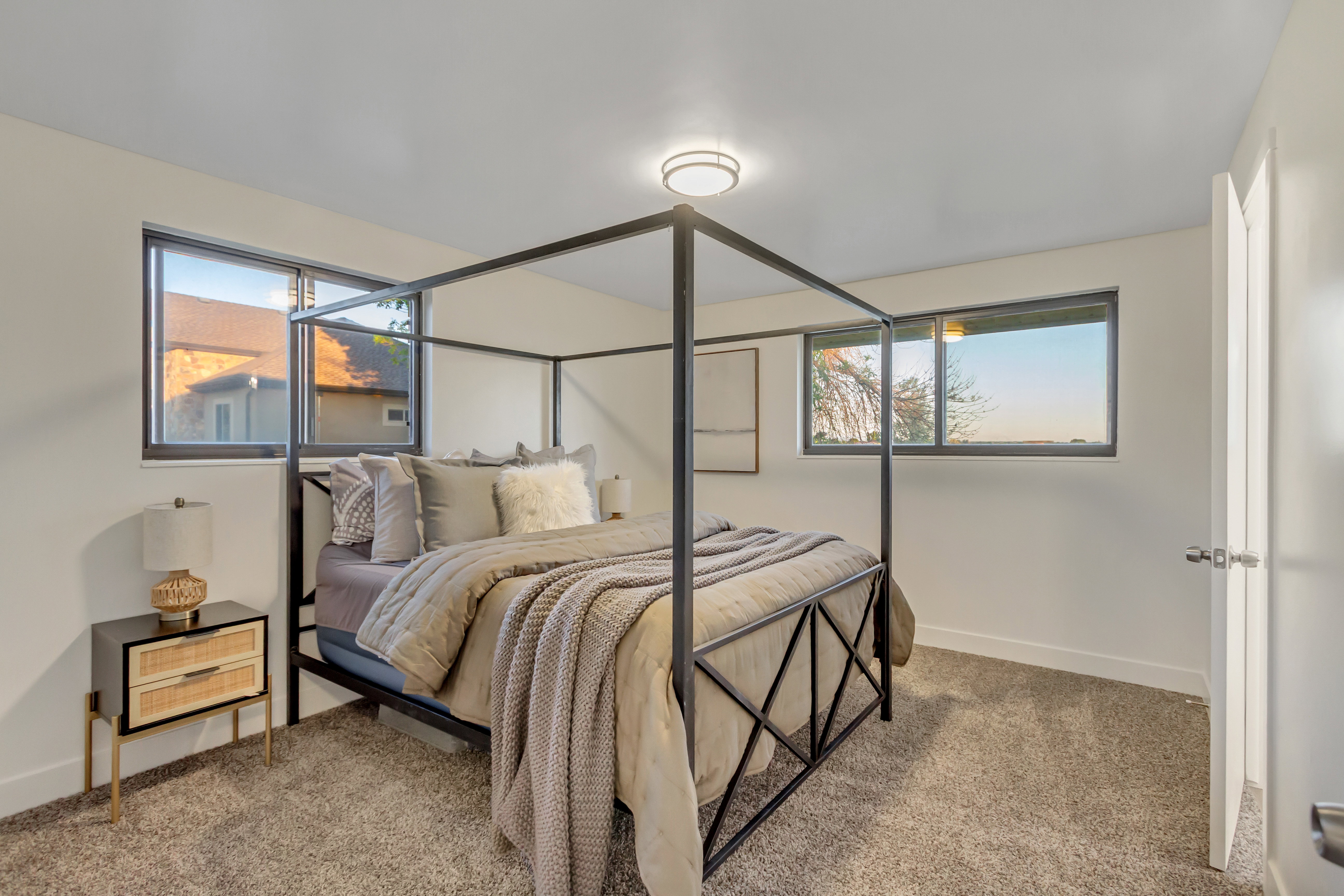 Carpeted bedroom featuring two windows with dark trim, a flush-mount ceiling light, white baseboards, and a white door with a silver handle