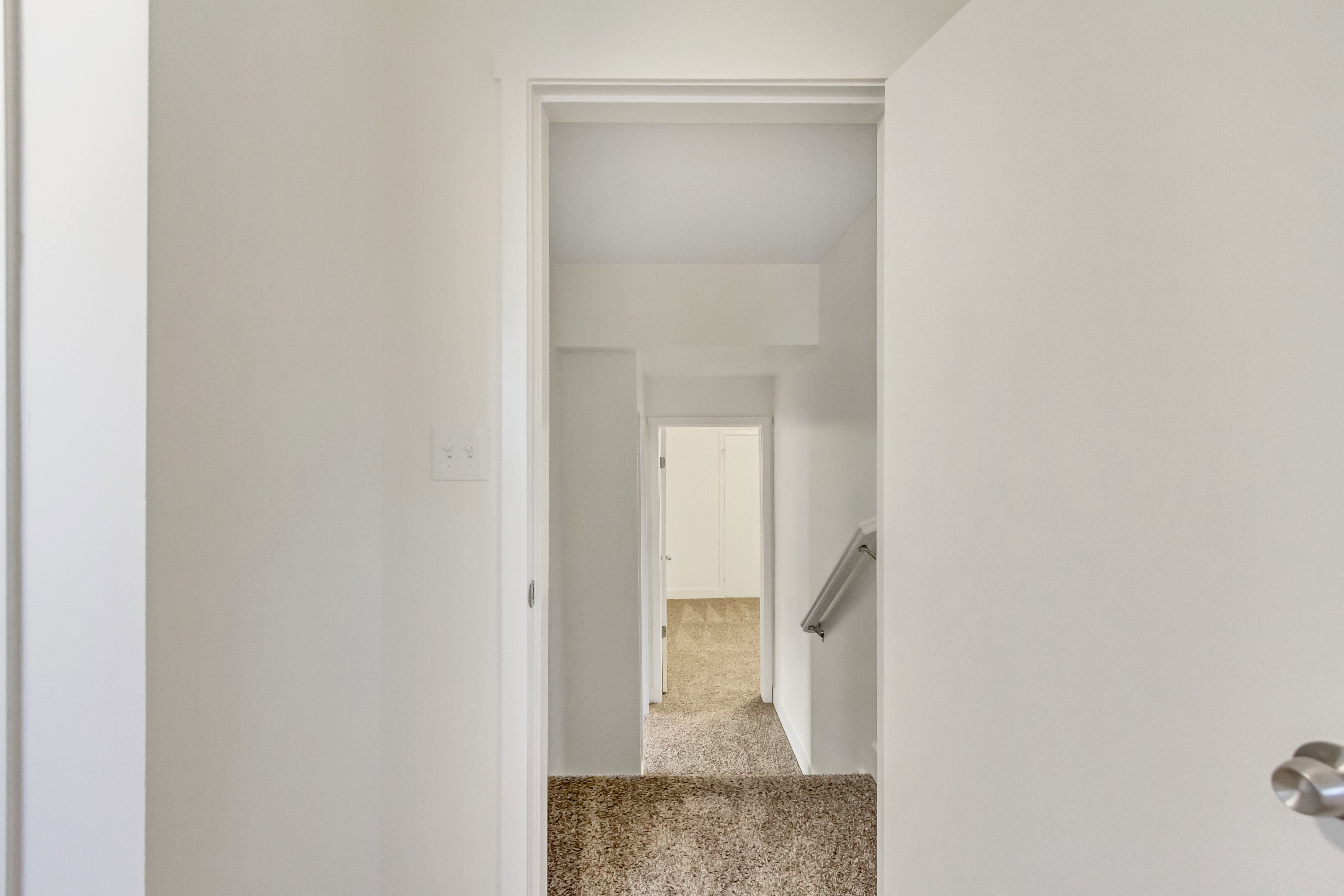 Entryway leading to carpeted stairs with a metal handrail