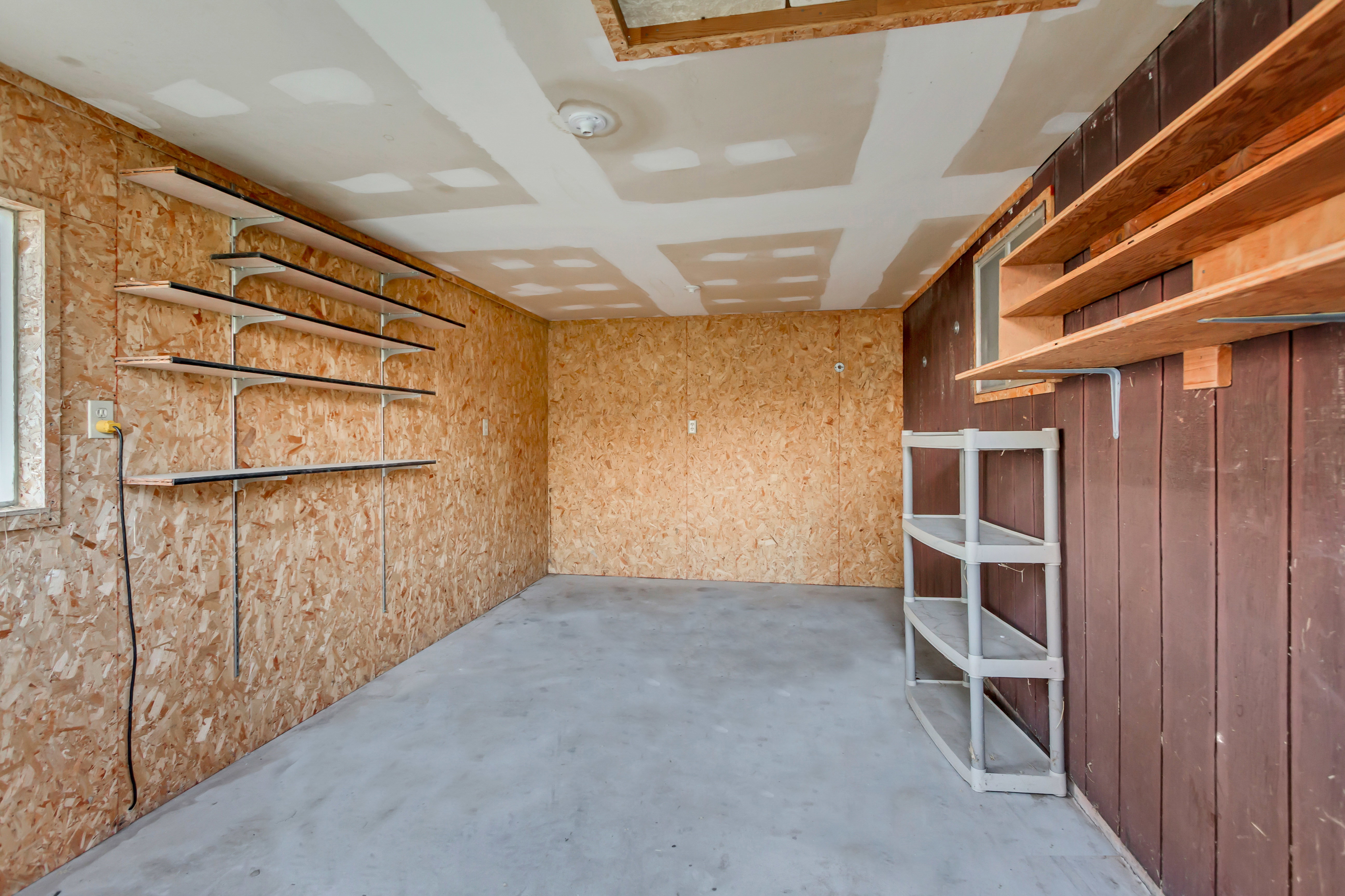 Utility room featuring concrete flooring, unpainted drywall ceiling, and textured wood-panel walls