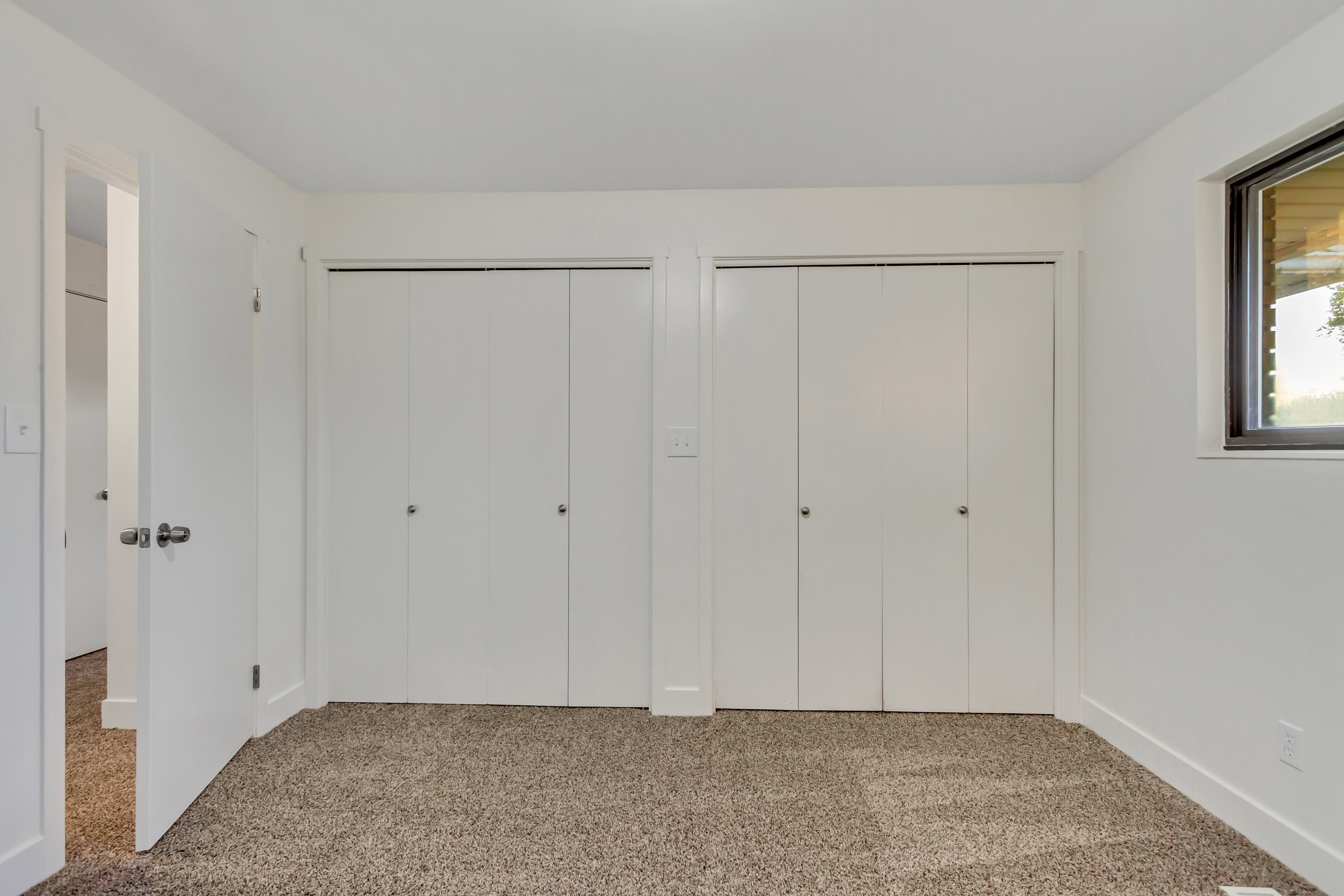 Interior room featuring neutral-toned carpeting, white walls, and two bi-fold closet doors