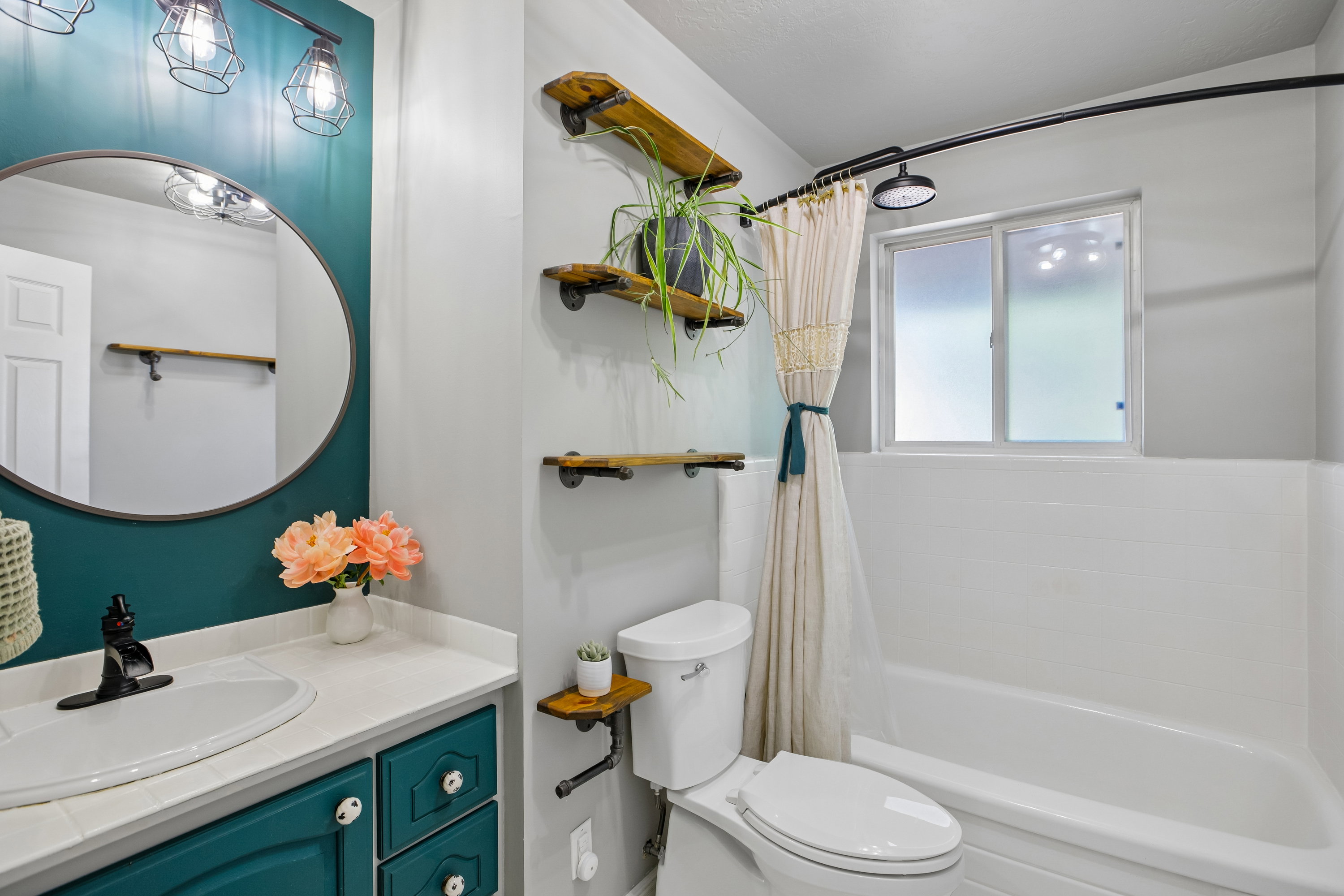 Bathroom featuring a teal vanity with white countertop, round mirror, and industrial-style light fixture