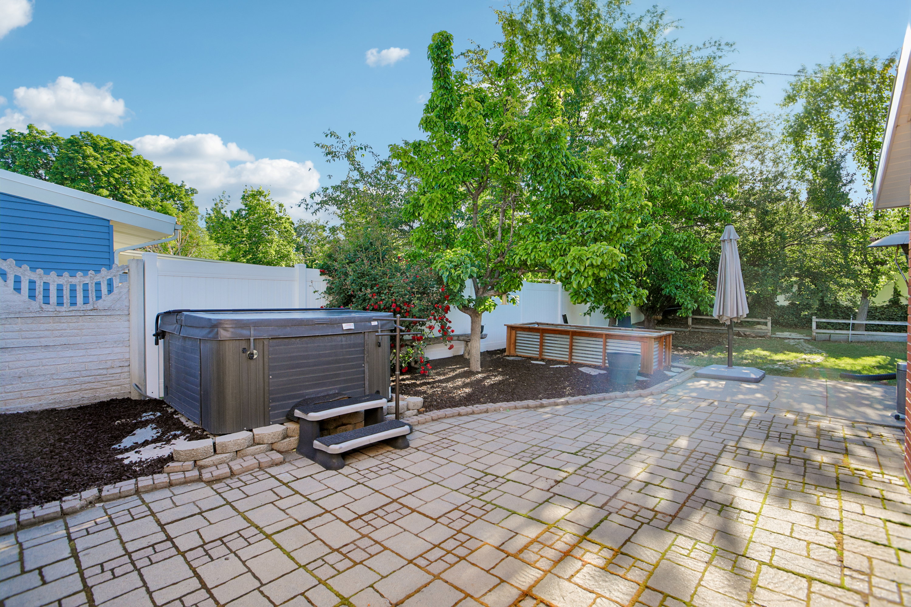 Outdoor hardscaping featuring a hot tub with steps, a paver patio, and mature trees
