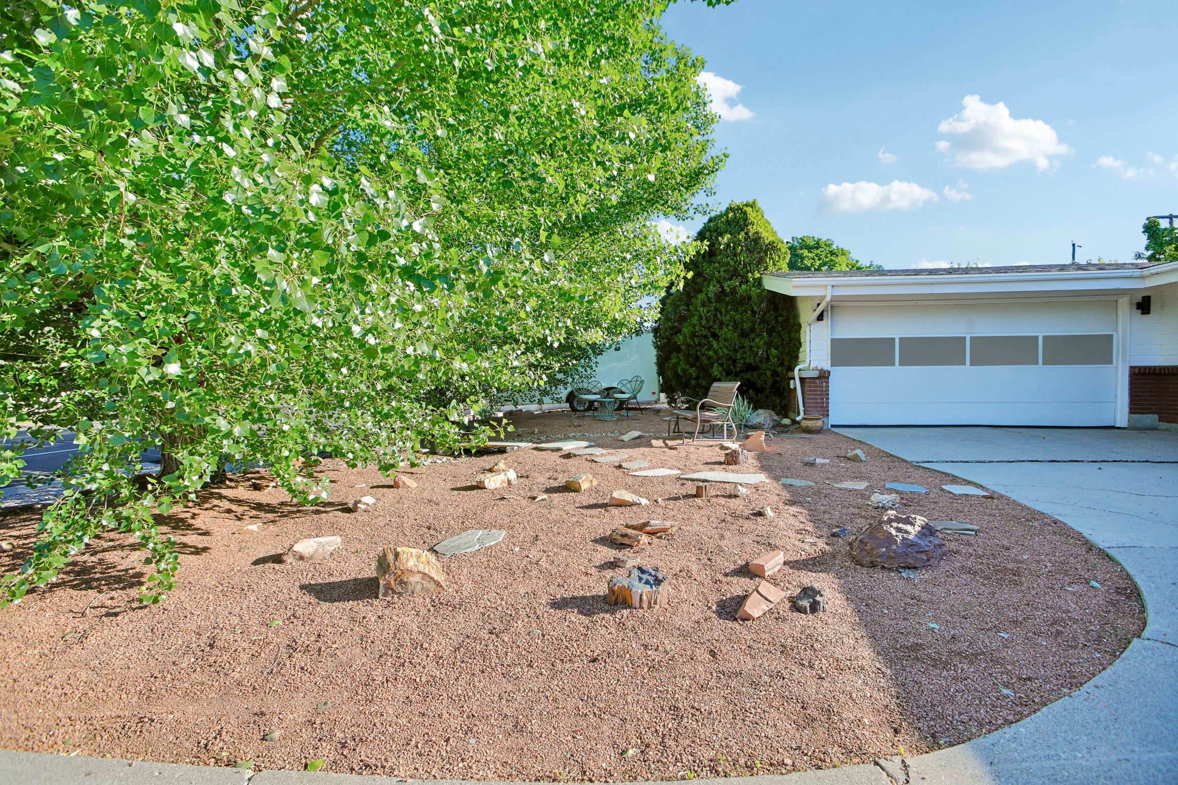 Exterior featuring a white overhead garage door with horizontal paneling, a concrete driveway, and a low-maintenance landscape design