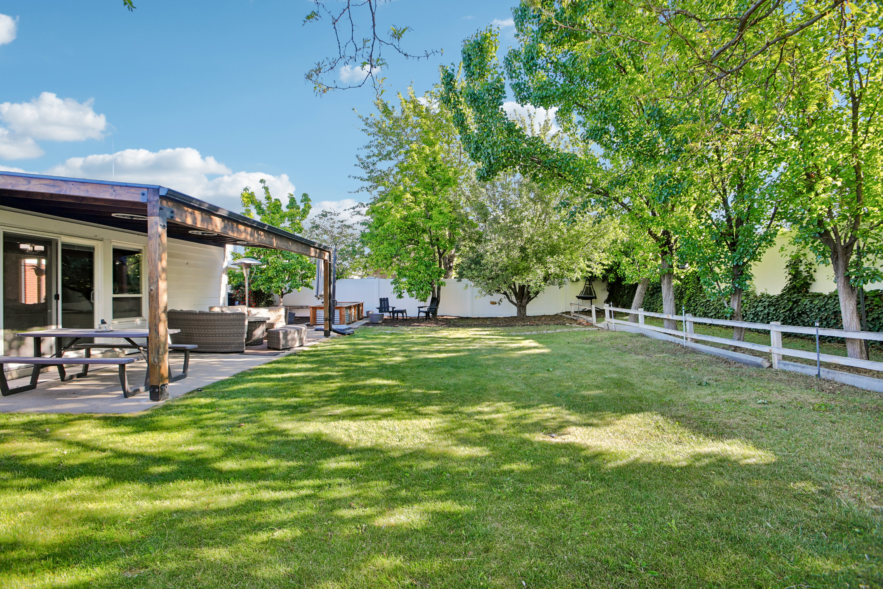 Expansive backyard featuring a large green lawn, mature trees, and a white fence