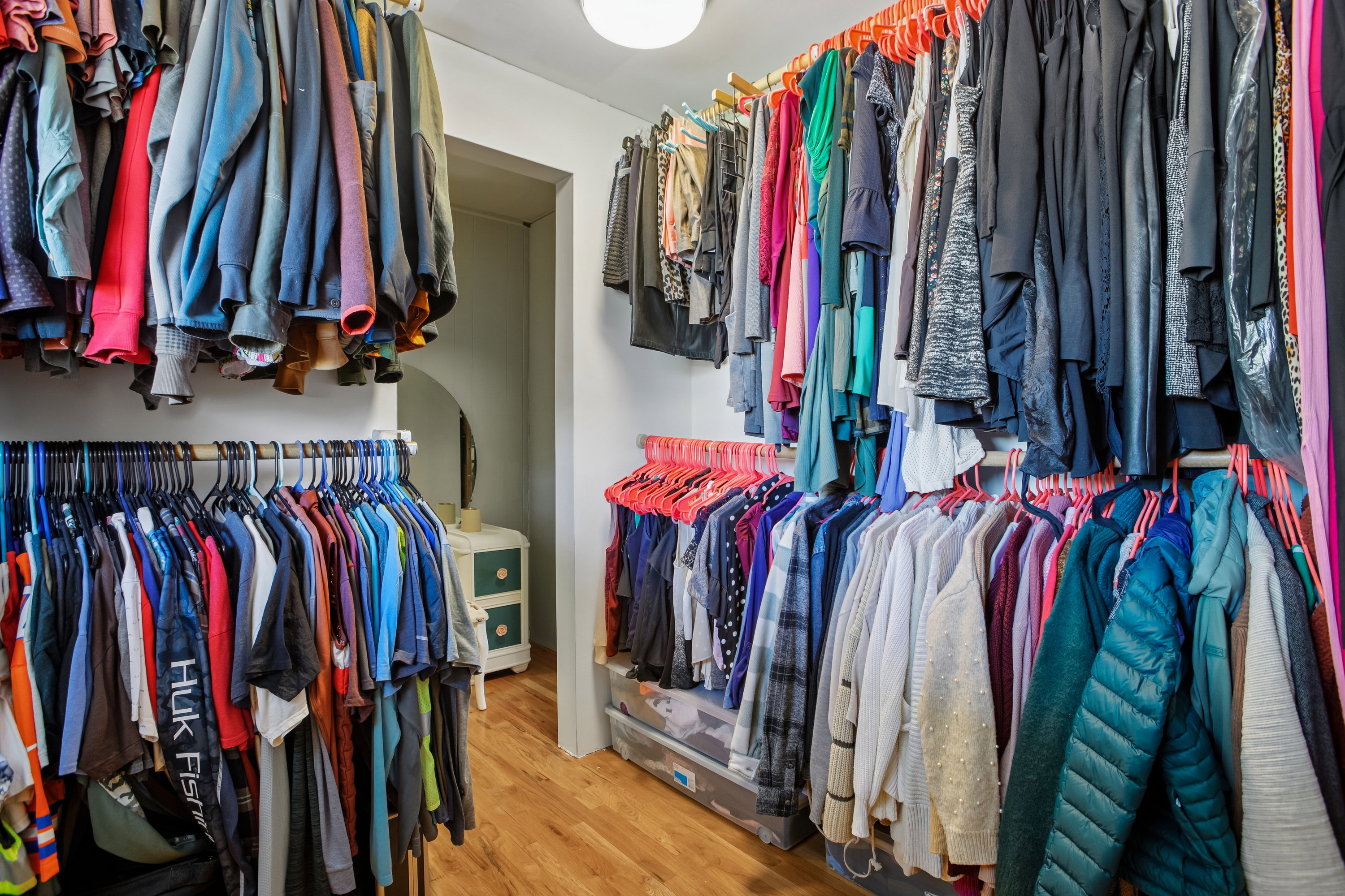 Walk-in closet featuring multiple clothing rods, upper storage shelving, wood-finish flooring, and a ceiling-mounted light fixture
