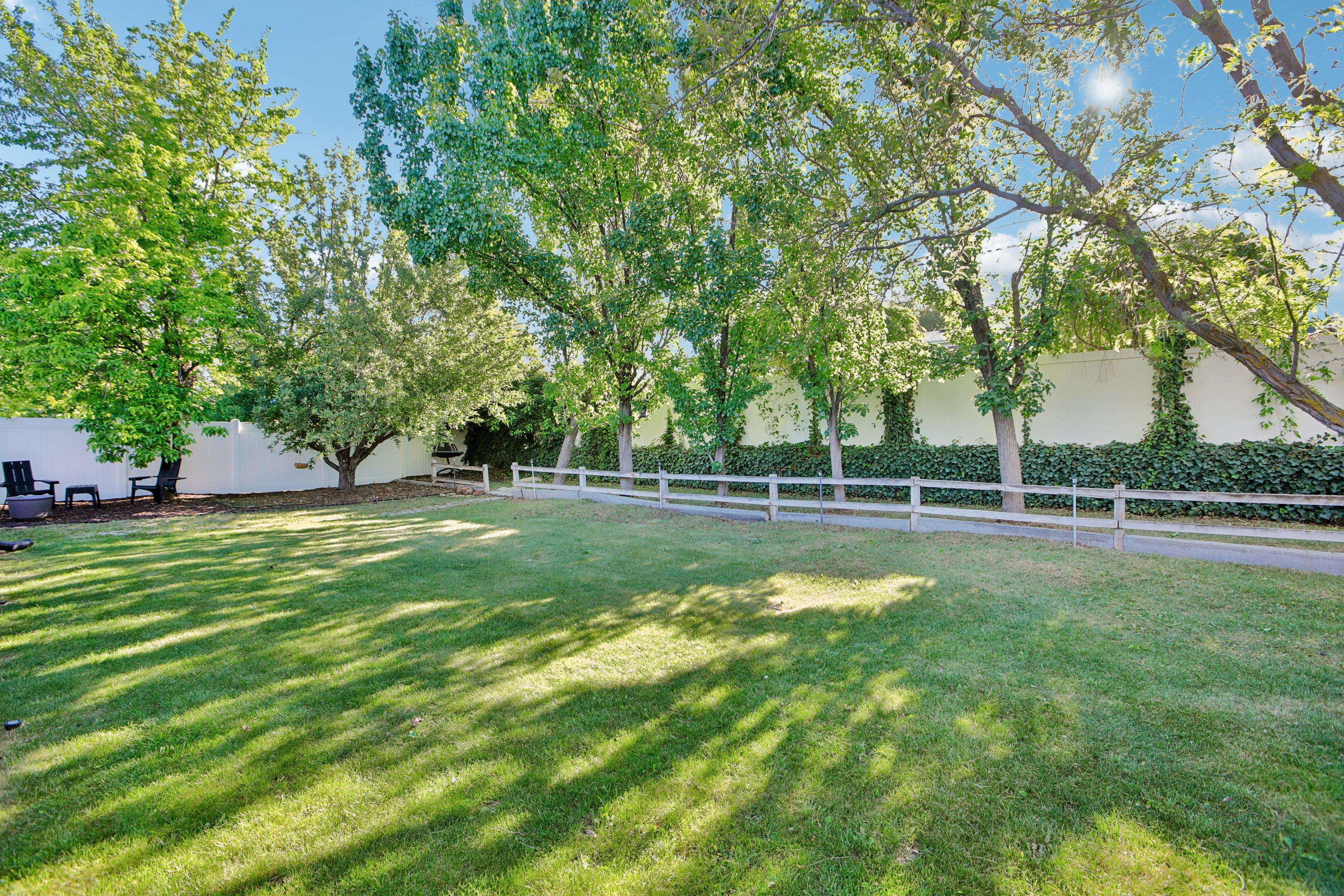 Expansive grassy area with mature trees and a white privacy fence