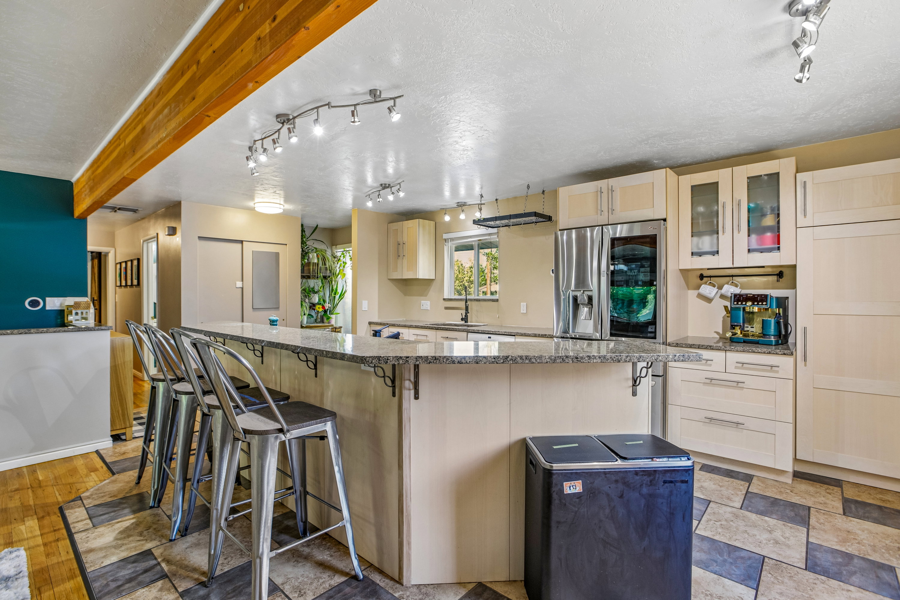 Kitchen featuring an expansive island with granite-finish countertop, light wood-finish cabinetry, stainless steel-finish refrigerator, and mixed tile flooring