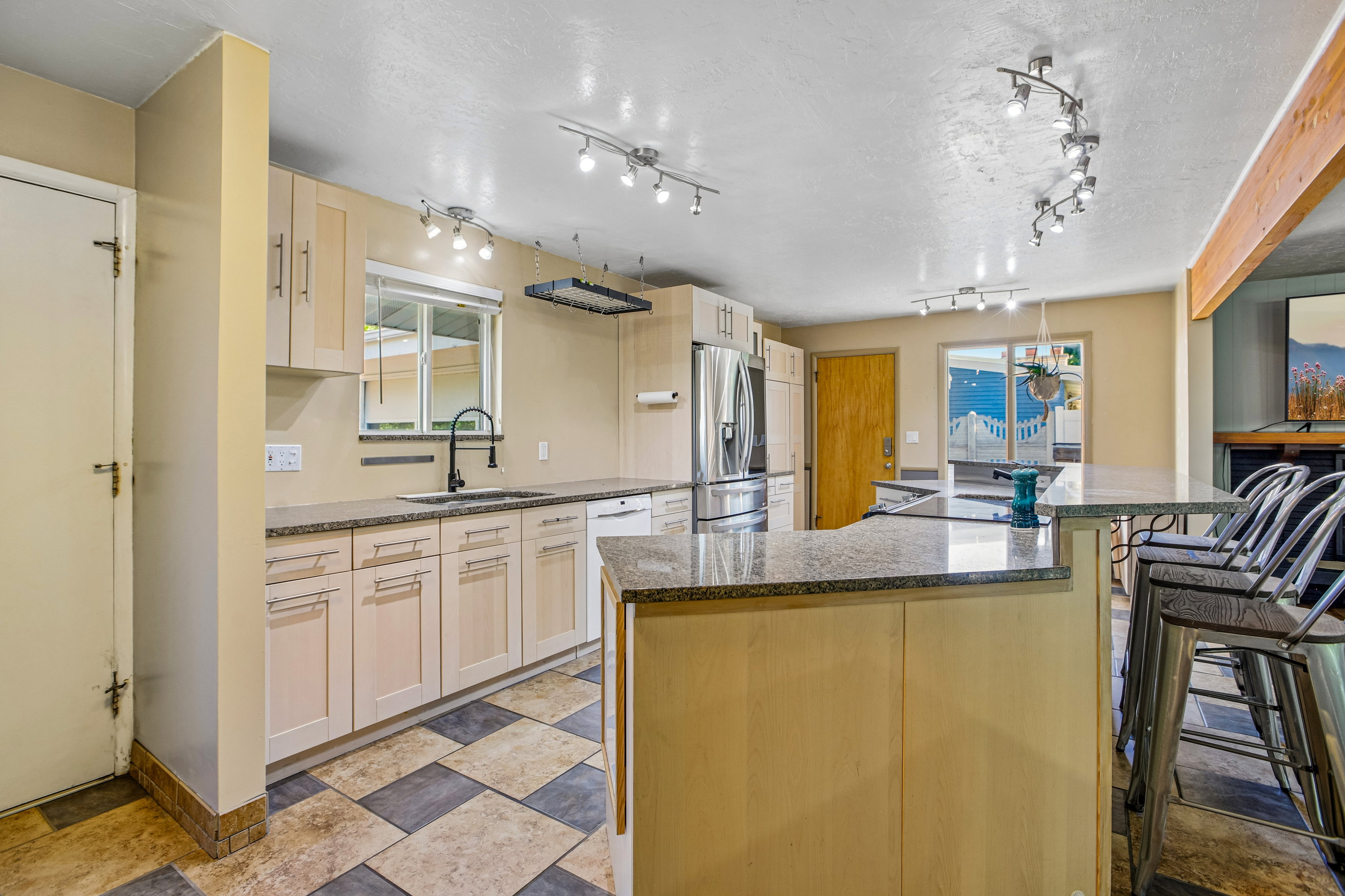 Kitchen featuring light wood cabinetry, granite-style countertops, stainless steel appliances, and a central island with bar seating