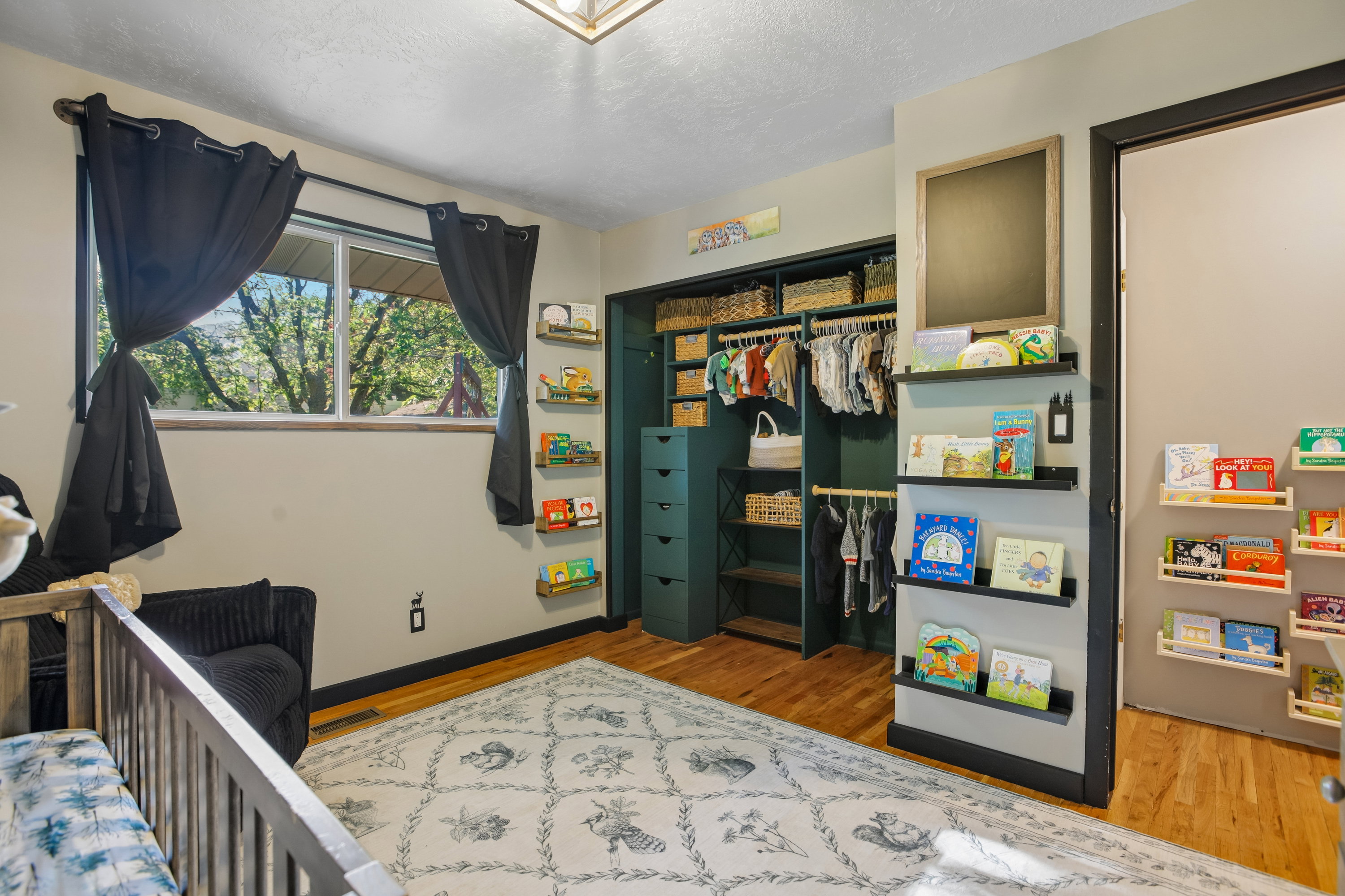 Room featuring wood-finish flooring, a window with natural light, a built-in closet system with drawers and hanging rods, and wall-mounted shelving units