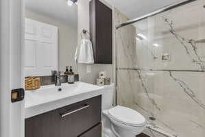 Primary Ensuite Bathroom featuring a contemporary floating vanity with an integrated sink, a dark wood-finish wall-mounted cabinet, a glass-enclosed shower with cultured marble surround, and a modern toilet