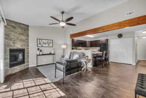 Open-concept living space featuring wood-finish flooring, a vaulted ceiling with a ceiling fan, and a gas fireplace with a stacked stone-look surround