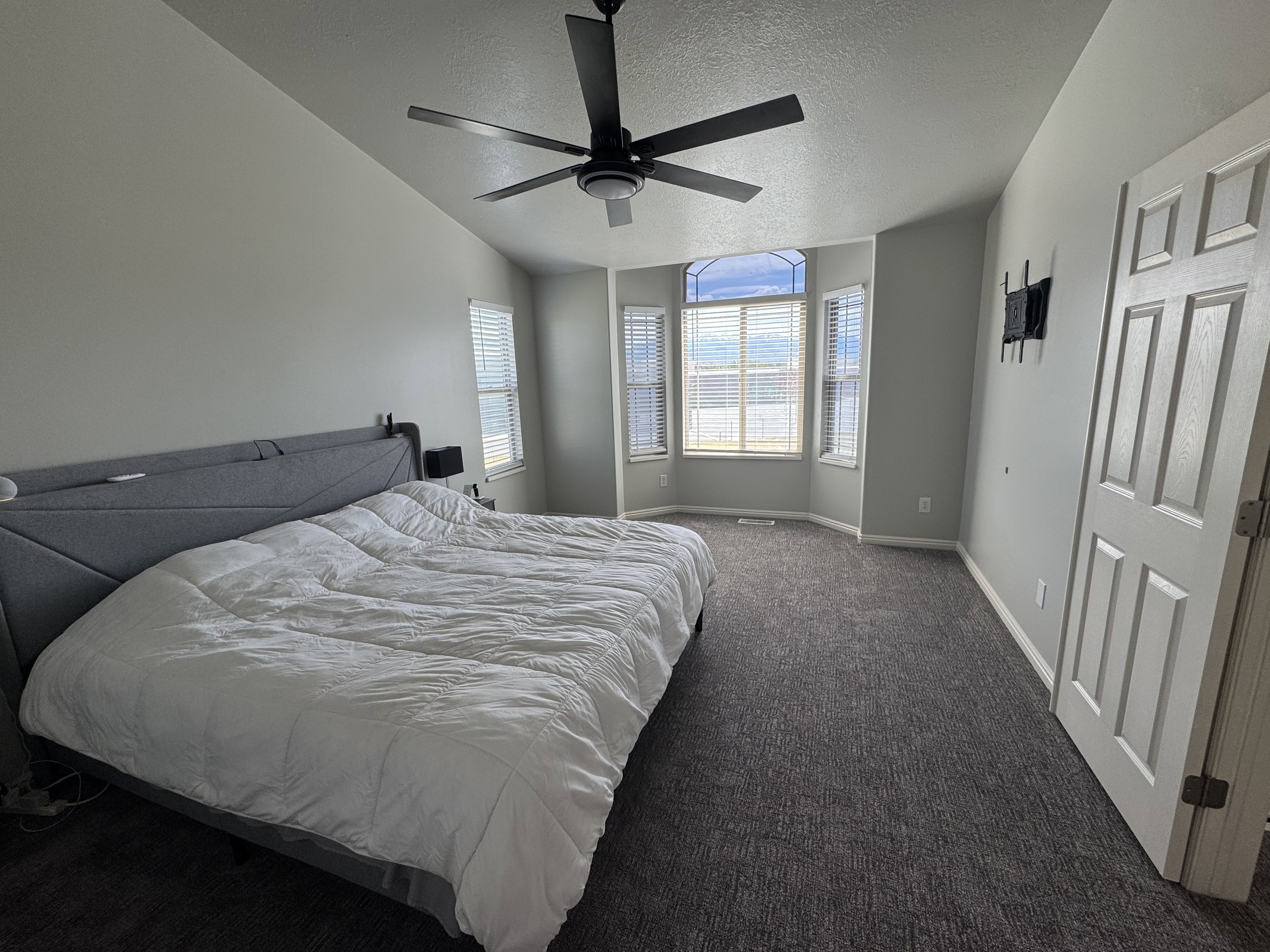 Room featuring a vaulted ceiling with a modern black ceiling fan, light gray wall paint, and dark patterned carpeting