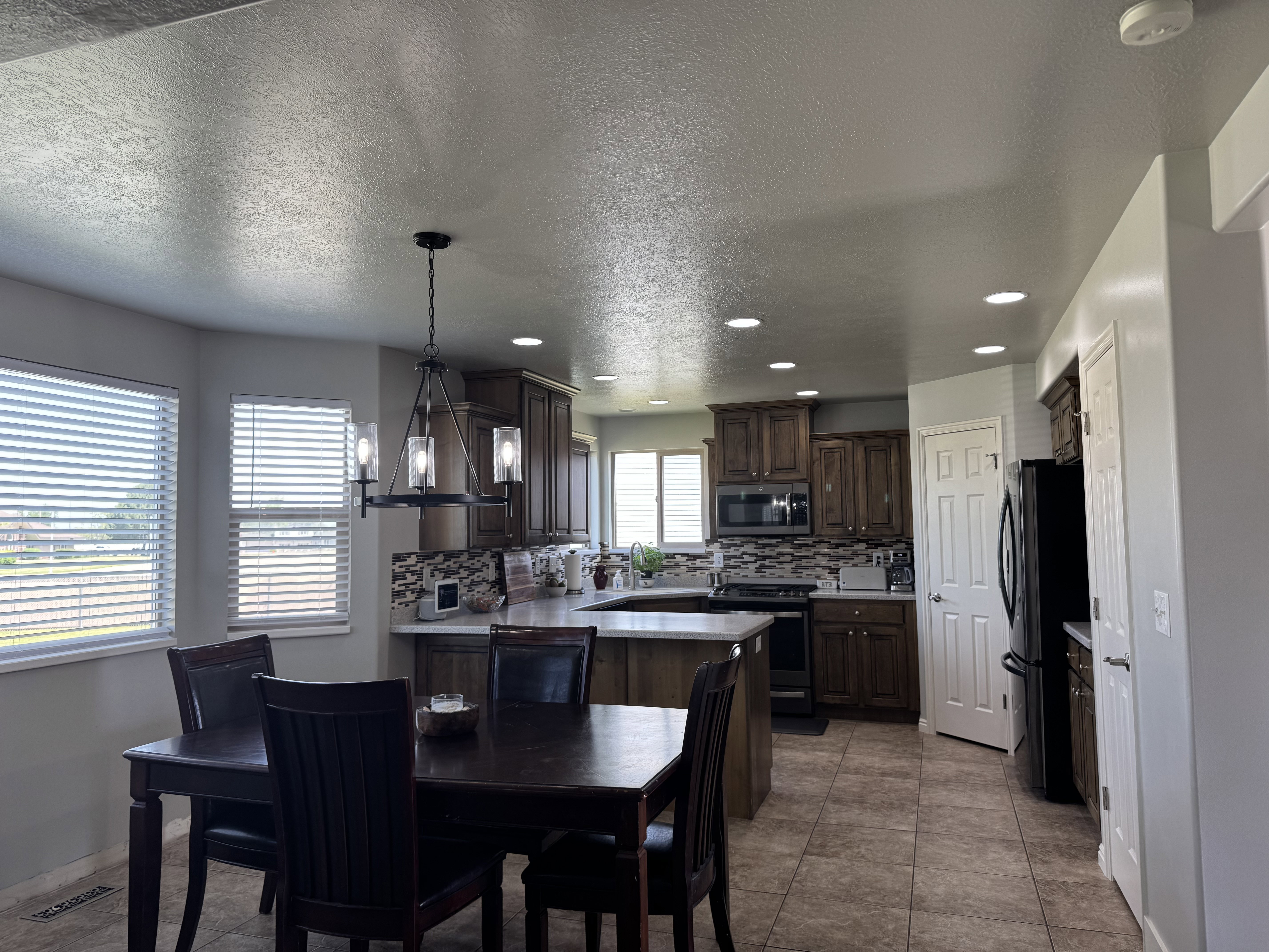 Kitchen and dining area featuring rich wood cabinetry, stainless steel microwave, black appliances, and a mosaic tile backsplash